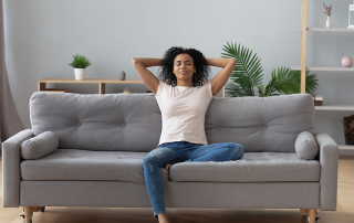 Happy young woman relaxes on grey couch and enjoys the benefits of an air exchanger