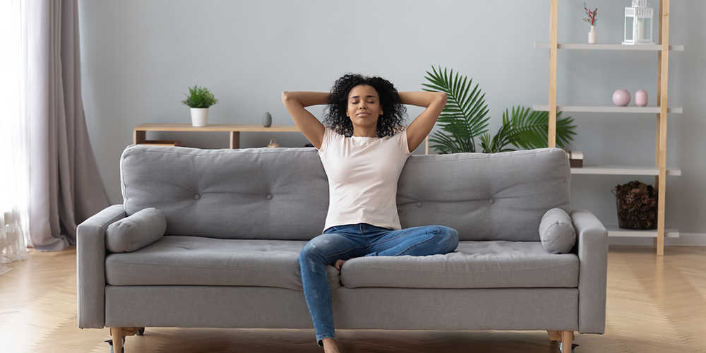 Happy young woman relaxes on grey couch and enjoys the benefits of an air exchanger