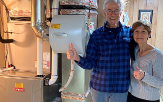 Satisfied homeowners give thumbs up next to furnace after using energy-efficiency tips.