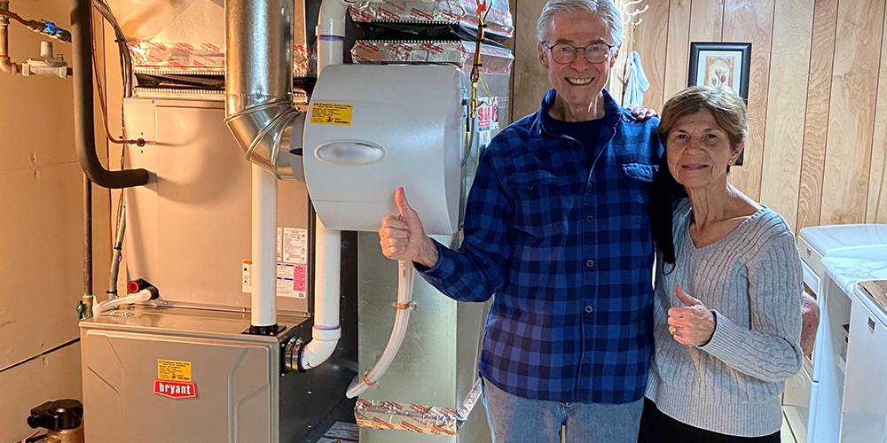 Satisfied homeowners give thumbs up next to furnace after using energy-efficiency tips.