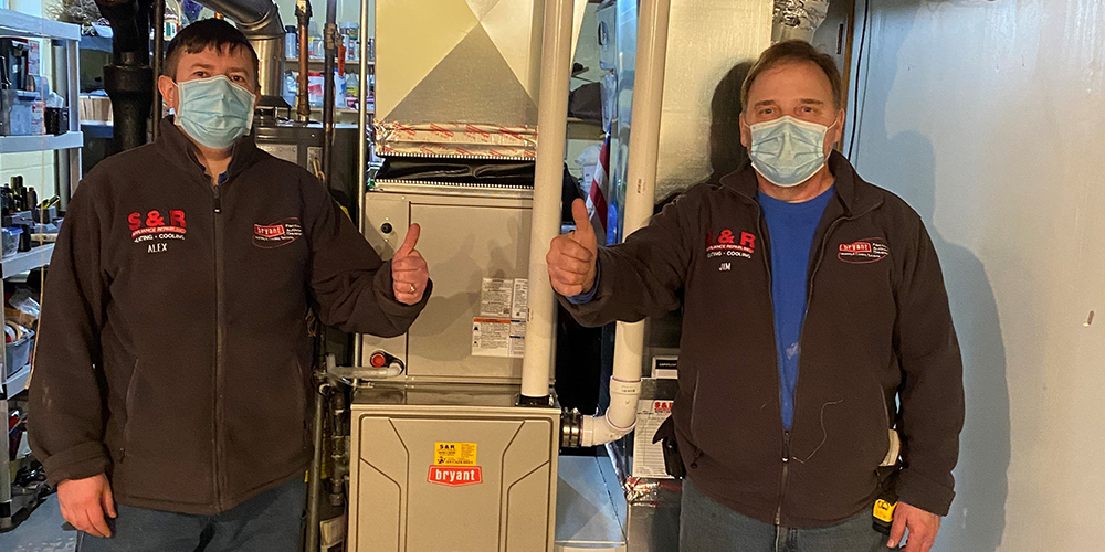 S&R techs give thumbs up near furnace after teaching homeowner how to improve air quality.